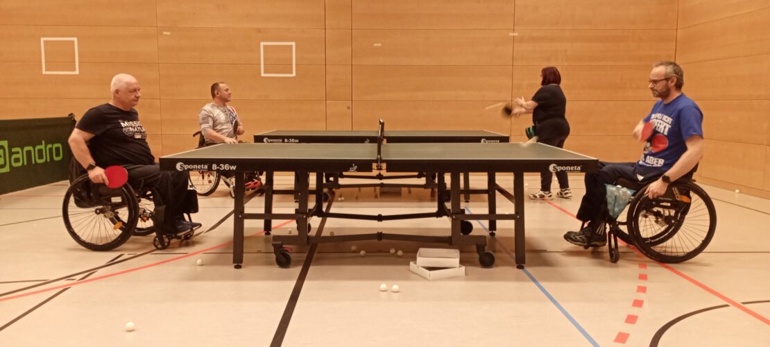 Rollstuhltischtennis inklusiv drei Rollstuhlfahrer und ein Fußgänger spielen gemeinsam Tischtennis